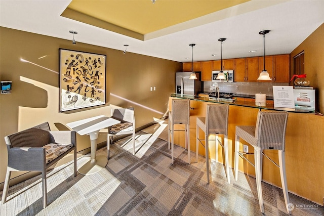 kitchen featuring a breakfast bar area, tasteful backsplash, decorative light fixtures, appliances with stainless steel finishes, and a tray ceiling