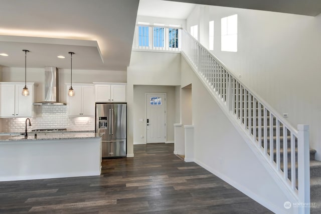 kitchen with high end fridge, white cabinets, light stone counters, and wall chimney exhaust hood