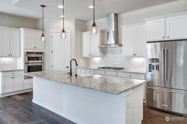 kitchen featuring pendant lighting, white cabinetry, an island with sink, stainless steel appliances, and wall chimney exhaust hood