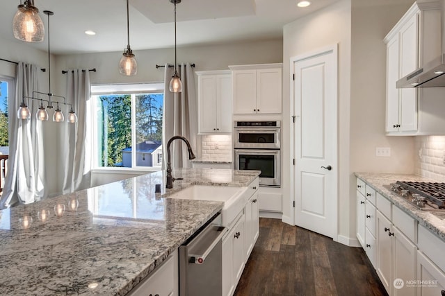 kitchen with appliances with stainless steel finishes, pendant lighting, white cabinetry, light stone counters, and wall chimney exhaust hood