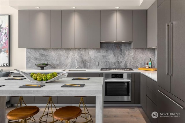 kitchen with sink, gray cabinets, a breakfast bar area, stainless steel appliances, and tasteful backsplash