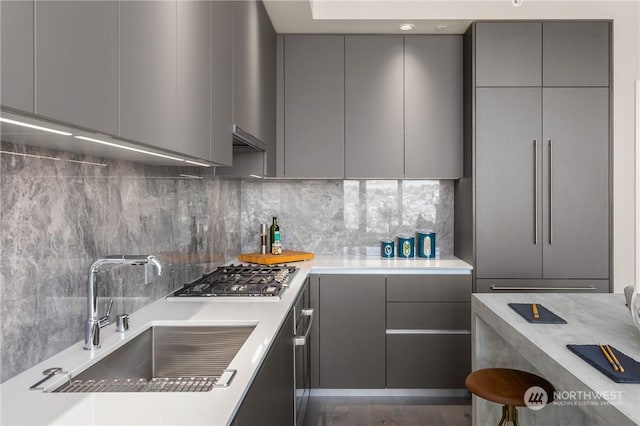 kitchen with sink, gray cabinets, stainless steel gas cooktop, and backsplash