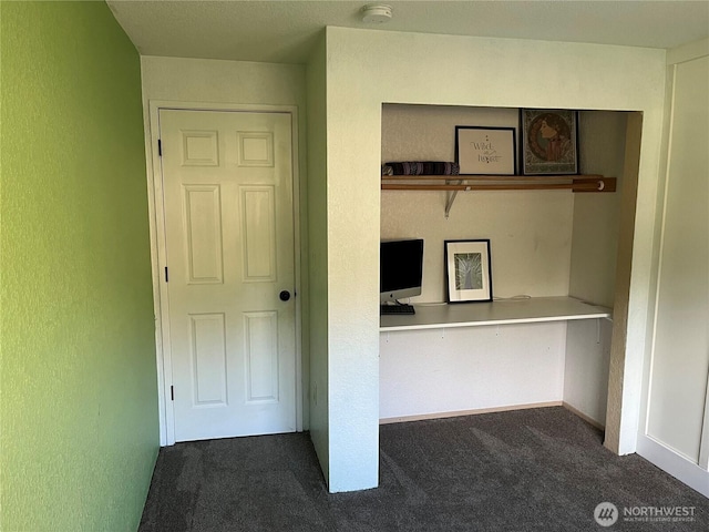 unfurnished office featuring dark carpet and a textured wall