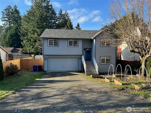 bi-level home with a garage, driveway, and fence