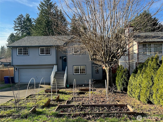 raised ranch with an attached garage, a shingled roof, fence, a garden, and concrete driveway