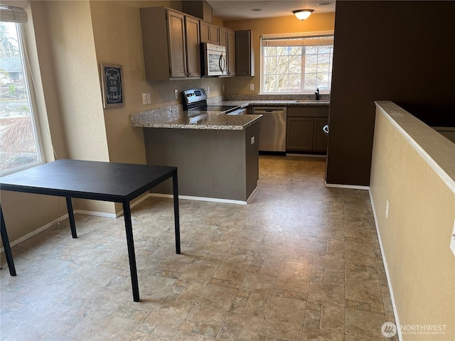 kitchen featuring a peninsula, baseboards, appliances with stainless steel finishes, and a sink