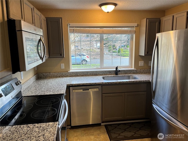 kitchen featuring appliances with stainless steel finishes, a sink, a textured ceiling, and light stone countertops