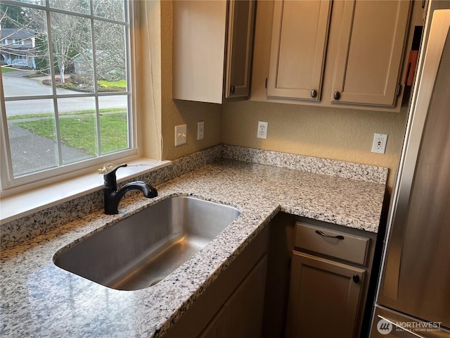 kitchen with a textured wall, light stone counters, a sink, and freestanding refrigerator