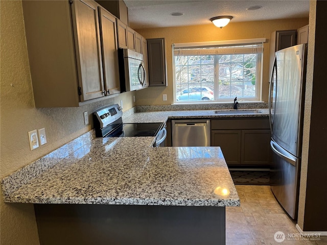 kitchen with a peninsula, stainless steel appliances, a sink, and a textured wall