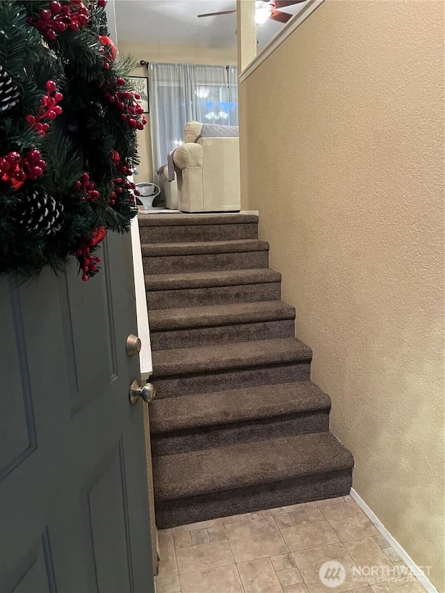 stairs featuring tile patterned flooring, a textured wall, baseboards, and ceiling fan