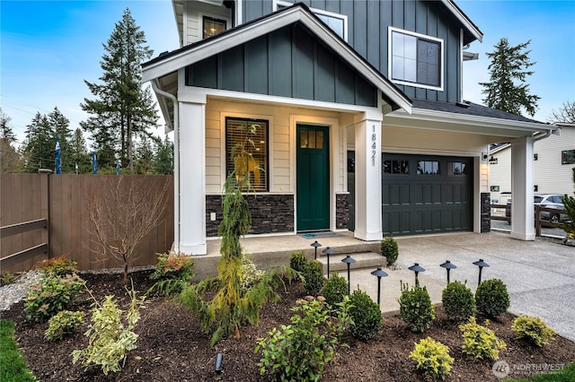 view of front facade featuring fence, concrete driveway, a garage, stone siding, and board and batten siding