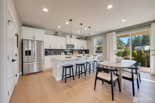 kitchen with backsplash, an island with sink, a kitchen breakfast bar, light wood-style floors, and stainless steel appliances