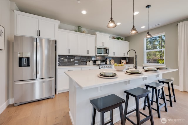 kitchen featuring tasteful backsplash, visible vents, an island with sink, appliances with stainless steel finishes, and white cabinetry