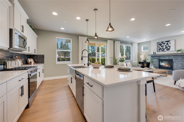 kitchen with a sink, decorative backsplash, a fireplace, stainless steel appliances, and a kitchen island with sink