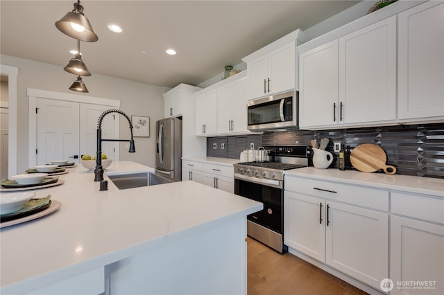 kitchen featuring light countertops, decorative backsplash, white cabinets, stainless steel appliances, and a sink