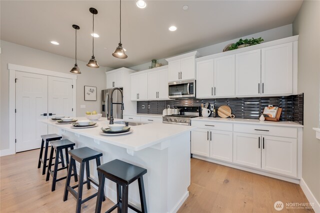 kitchen with stainless steel appliances, a breakfast bar area, an island with sink, and white cabinets