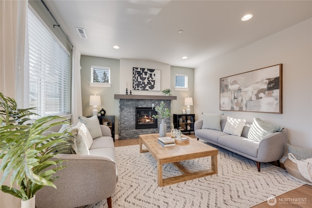 living area featuring recessed lighting, a glass covered fireplace, a healthy amount of sunlight, and wood finished floors