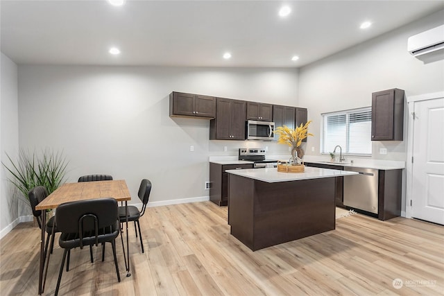 kitchen with sink, a center island, light wood-type flooring, a wall unit AC, and stainless steel appliances