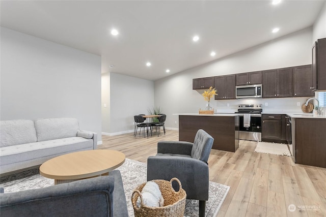 living room featuring high vaulted ceiling, sink, and light wood-type flooring