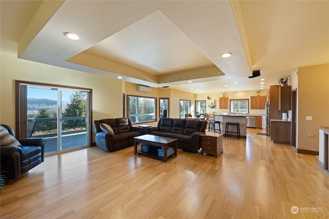 living room featuring light hardwood / wood-style flooring, a wall unit AC, and a tray ceiling