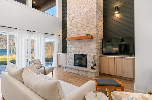 living room featuring a high ceiling, a stone fireplace, and light hardwood / wood-style flooring