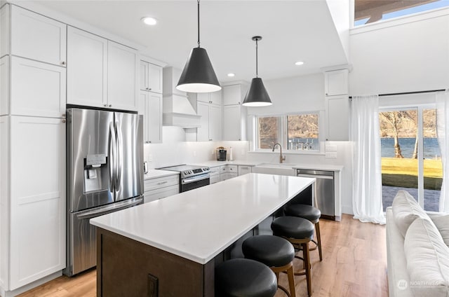 kitchen with stainless steel appliances, white cabinetry, a kitchen island, and light hardwood / wood-style flooring