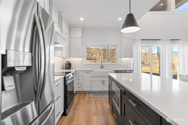 kitchen featuring sink, light hardwood / wood-style flooring, white cabinetry, hanging light fixtures, and stainless steel appliances