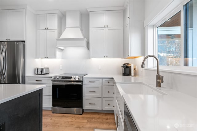 kitchen with premium range hood, white cabinetry, stainless steel appliances, and light hardwood / wood-style flooring