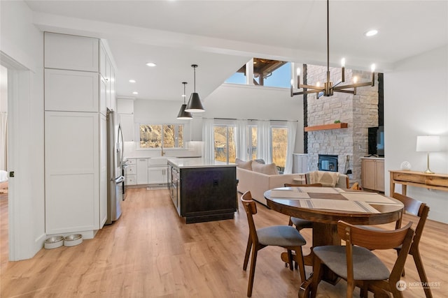 dining area featuring an inviting chandelier, beam ceiling, high vaulted ceiling, light hardwood / wood-style floors, and a stone fireplace