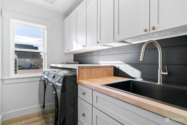 clothes washing area with cabinets, washing machine and dryer, wood-type flooring, and sink