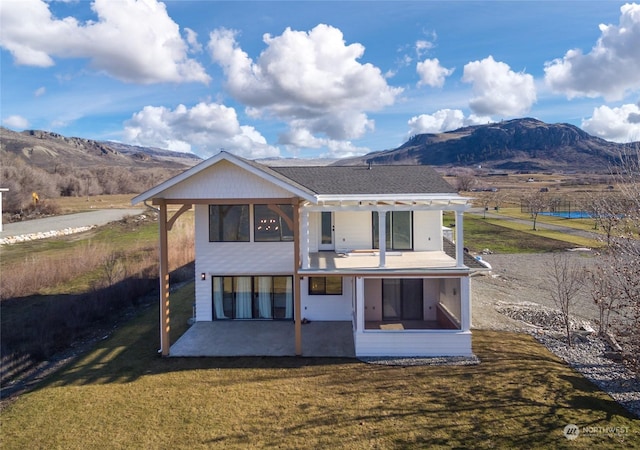 rear view of property featuring a mountain view, a patio, and a lawn