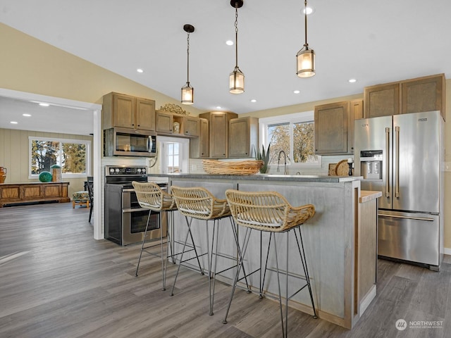 kitchen with appliances with stainless steel finishes, a kitchen breakfast bar, a kitchen island, pendant lighting, and hardwood / wood-style floors