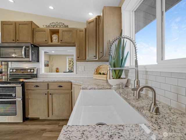 kitchen featuring lofted ceiling, stainless steel appliances, light hardwood / wood-style floors, and backsplash