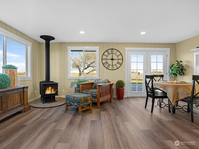 sitting room featuring french doors, plenty of natural light, wood-type flooring, and a wood stove