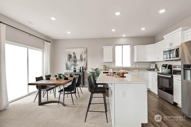 kitchen with dark wood-type flooring, a breakfast bar area, appliances with stainless steel finishes, white cabinetry, and a center island