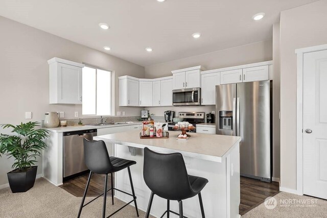 kitchen with appliances with stainless steel finishes, sink, white cabinets, a kitchen bar, and a center island