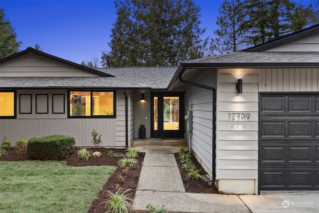 exterior entry at dusk featuring a garage and a yard