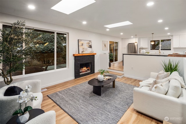 living room featuring light hardwood / wood-style flooring, a brick fireplace, a skylight, and sink