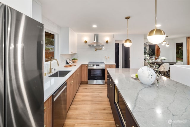 kitchen with pendant lighting, appliances with stainless steel finishes, light stone countertops, white cabinets, and wall chimney exhaust hood