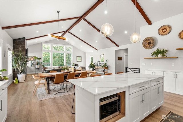 kitchen featuring beamed ceiling, white cabinetry, light stone countertops, and pendant lighting