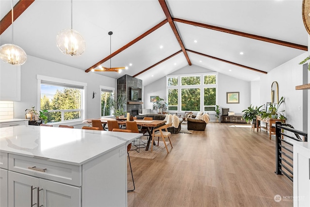 kitchen with a breakfast bar area, hanging light fixtures, beam ceiling, light hardwood / wood-style floors, and a large fireplace