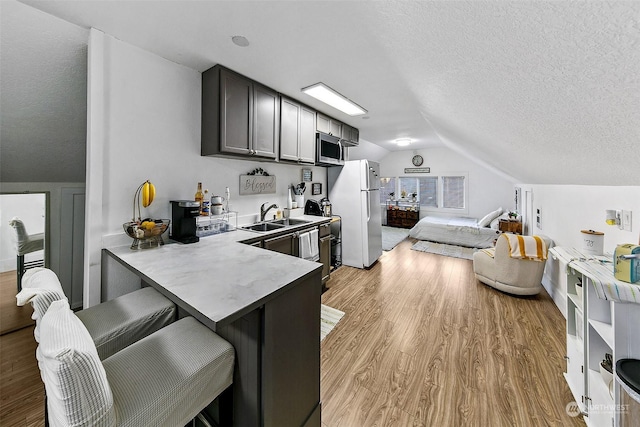 kitchen with lofted ceiling, sink, white fridge, kitchen peninsula, and light wood-type flooring