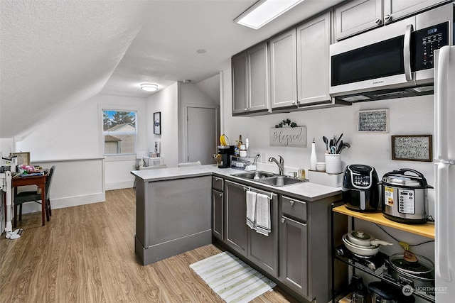 kitchen with vaulted ceiling, sink, gray cabinetry, and kitchen peninsula