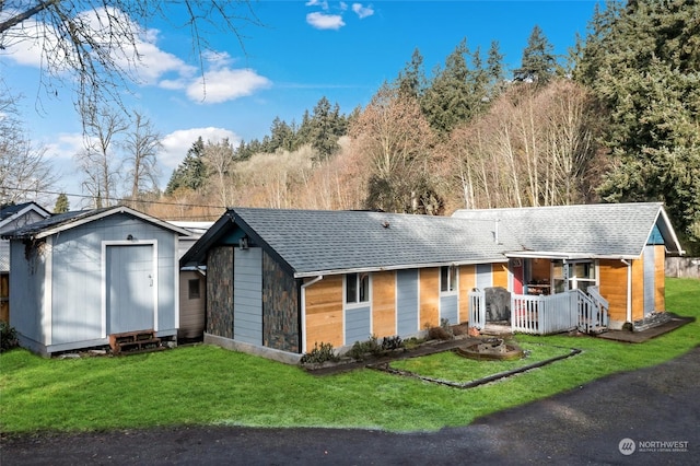 ranch-style house with a shingled roof, an outbuilding, and a front yard