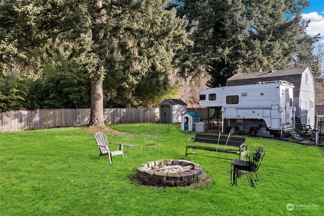 view of yard featuring a storage shed, a fenced backyard, a fire pit, and an outdoor structure