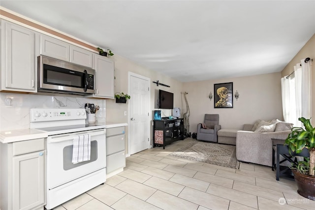 kitchen with light countertops, white electric range, stainless steel microwave, decorative backsplash, and open floor plan