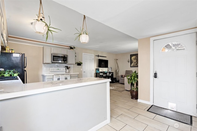 kitchen featuring white range with electric stovetop, stainless steel microwave, freestanding refrigerator, decorative light fixtures, and light countertops