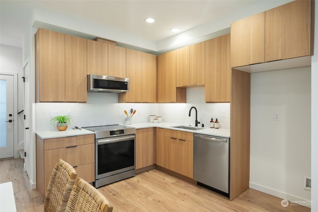 kitchen with light brown cabinetry, sink, backsplash, stainless steel appliances, and light wood-type flooring