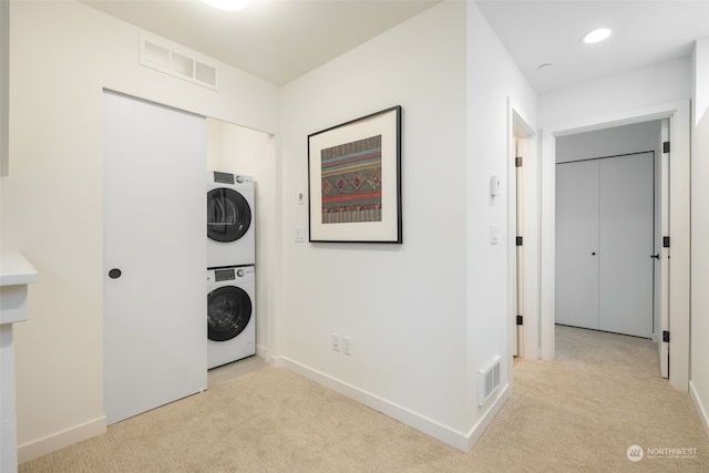 clothes washing area with stacked washer / dryer and light carpet