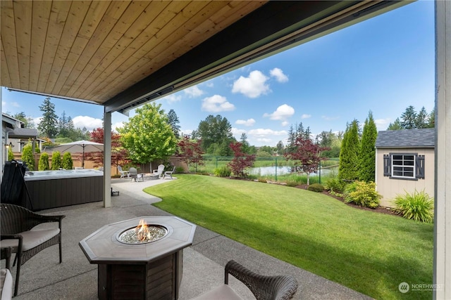 view of patio with a water view, an outdoor fire pit, a hot tub, and a storage unit